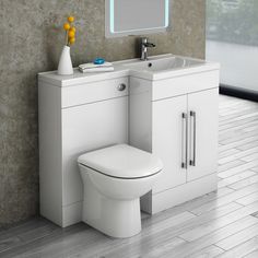 a white toilet sitting next to a sink and mirror in a room with wooden floors