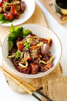 a white bowl filled with food next to chopsticks on a wooden cutting board