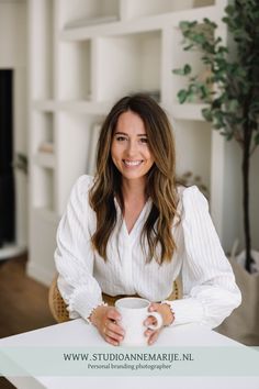 a woman sitting at a table with a cup in her hand and smiling for the camera