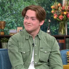 the young man is sitting down talking to someone on the television show, and he's wearing a green shirt