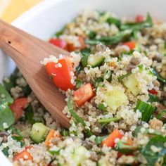 a white bowl filled with rice and vegetables next to a wooden spoon on top of a table