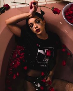 a woman laying in a bathtub with rose petals on the floor next to her