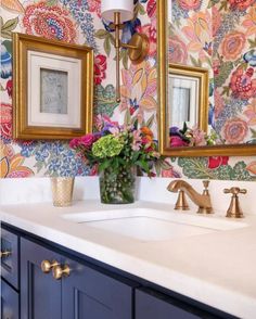 a bathroom sink with two mirrors above it and flowers on the wall next to it