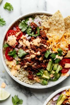 two bowls filled with mexican food and tortilla chips next to lime wedges