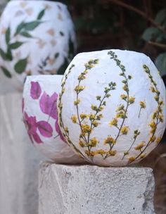 three white vases with flowers painted on them sitting next to each other in front of some bushes