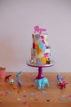 there is a cake on the table with toy animals around it and confetti