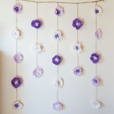 purple and white crocheted flowers hanging from a string in front of a wall