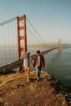 two people walking on the side of a hill next to a bridge