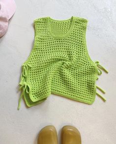 a pair of yellow rubber shoes next to a green knitted vest