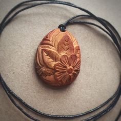 a necklace with a wooden flower on it sitting on a table next to a black cord