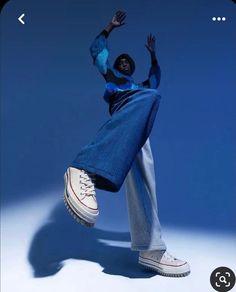 a person in blue jeans and white sneakers is doing a dance move with their hands up