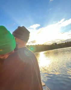 two people are sitting on a boat in the water, one is wearing a green hat