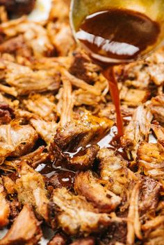 a spoon pouring sauce onto some food that is on top of a pan filled with meat