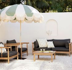 two chairs and an umbrella in front of a white wall with potted plants on it