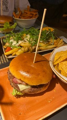 a large hamburger sitting on top of an orange plate next to french fries and corn