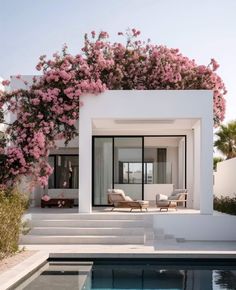 a white house with pink flowers growing on the roof and pool in front of it