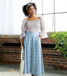 a woman standing in front of a window wearing a white top and blue plaid pants