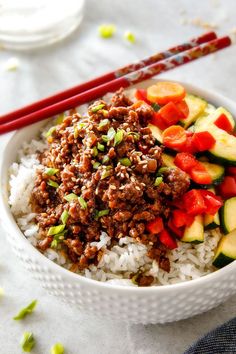 a bowl filled with rice, meat and veggies next to chopsticks