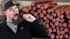 a man holding a stick in his mouth next to a pile of sausages that are stacked on top of each other