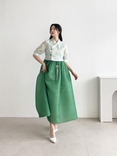 a woman standing in front of a white wall wearing a green skirt and shirt with pockets