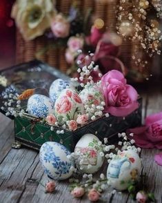 an arrangement of flowers and eggs on a wooden table next to a basket with pink roses