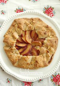 an apple pie on a white plate topped with almonds and sliced peaches, sitting on a floral tablecloth