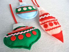 three christmas ornaments hanging from red and green strings on a white surface with snow in the background