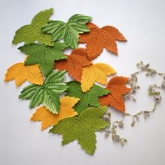 crocheted autumn leaves are arranged on a white surface with green, orange and yellow stems