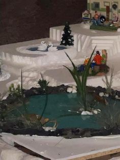 a miniature snow scene with people sitting on the bench and in the background is a pond