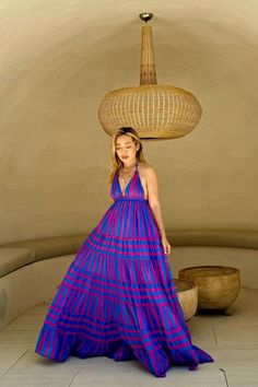 a woman in a purple and blue dress standing next to a large basket on top of her head