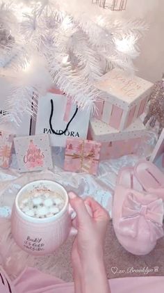 a person is holding a cup of coffee in front of christmas decorations and gifts on the floor