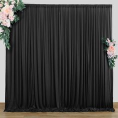 a black backdrop with pink flowers and greenery on the top is ready for an event