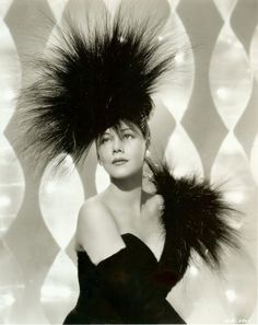 black and white photograph of a woman with large feathers on her head, wearing a dress