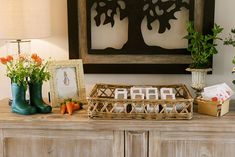 a wooden dresser topped with vases filled with flowers next to a painting and framed pictures