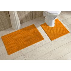 two orange bath mats sitting on top of a bathroom floor next to a white toilet