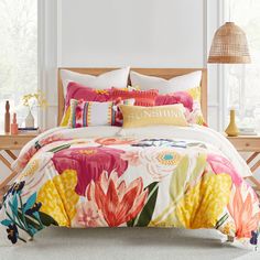 a bed with colorful flowers on it in a room next to a lamp and window