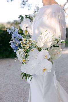 a woman wearing a white dress holding a bouquet of blue and white flowers in her hand