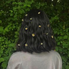 the back of a woman's head with daisies in her hair, against a backdrop of greenery