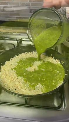 someone pouring green liquid into a pan on top of a stove with food in it