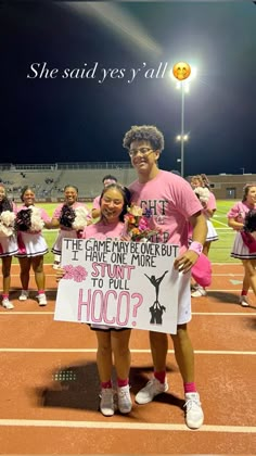 two girls in pink shirts are holding signs on the sidelines with cheerleaders behind them