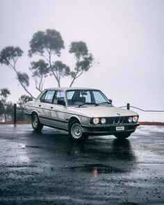 an old car is parked on the wet parking lot with trees in the back ground