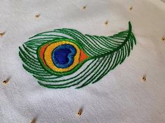 a close up of a peacock feather embroidered on a white shirt with gold sequins