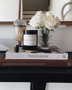 two books on a table with flowers in a vase next to it and a candle