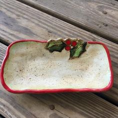 a red and white ceramic dish with holly leaves on it sitting on a wooden bench