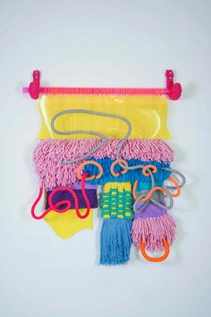 an assortment of colorful objects are hanging on a white wall with plastic handles and strings