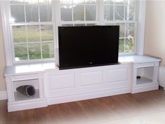 a flat screen tv sitting on top of a white shelf in front of a window