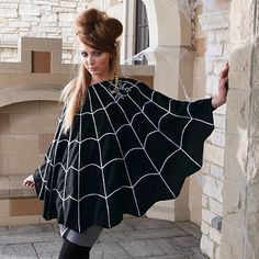 a woman standing in front of a brick wall wearing a black and white spider web cape