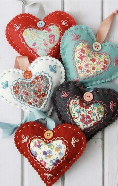 four heart shaped ornaments are hanging on a white wooden wall with ribbons and buttons in the shape of hearts