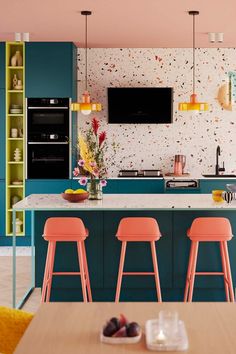 a kitchen with blue cabinets and pink stools in the foreground is a tv mounted on the wall