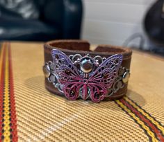 "One of a kind, upcycled leather bracelet made from used belts, upholstery scraps, and artistic findings. Every cuff is unique and made to wear and weather well.  Like high quality boots or your favorite leather journal, these cuffs get softer and more supple over time. The individual designs all start with the leather.  I use vintage belts, leather scraps, WW2 rifle holsters, and old horse bridles.  Each piece speaks to me, and informs the direction for the finished piece.  Adornments include found objects, printed leather, metal studs, gemstones, buttons - anything that will bring the cuff to life and make it a statement piece unlike any other. I prefer using a button & elastic closure when possible, as it makes the cuff fully adjustable.  It's a more labor and cost intensive process, bu High Quality Boots, Horse Bridle, Upcycled Leather, Leather Scraps, Bridles, Vintage Belts, Leather Journal, Leather Cuffs, Beaded Lace